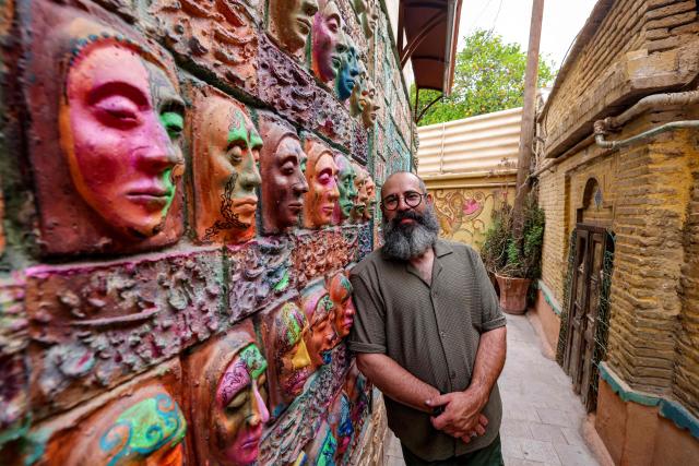 (FILES) Adel Yazdi, an Iranian artist who has transformed an alley in one of the old neighbourhoods of Shiraz into an open air permanent art gallery, stands next to one of his high reliefs in the central Iranian city on May 14, 2024. Yazdi's work has over the years stood out in Shiraz where graffiti and murals are rare, becoming a social media sensation and a tourist attraction. (Photo by ATTA KENARE / AFP)