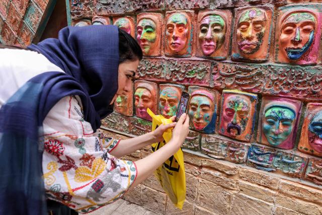 (FILES) A woman snaps a picture of a high relief by Adel Yazdi, an Iranian artist who has transformed an alley in one of the old neighbourhoods of Shiraz into an open air permanent art gallery, displayed on a wall in the central Iranian city on May 14, 2024. Yazdi's work has over the years stood out in Shiraz where graffiti and murals are rare, becoming a social media sensation and a tourist attraction. (Photo by ATTA KENARE / AFP)