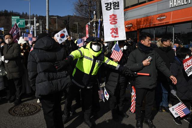 A police officer monitors traffic flow while keep watch over supporters of South Korea's impeached President Yoon Suk Yeol gathered near his residence in Seoul on January 3, 2025. South Korean investigators attempted to arrest impeached President Yoon at his residence on January 3 over a failed martial law bid, but security forces were blocking their efforts. (Photo by Philip FONG / AFP)