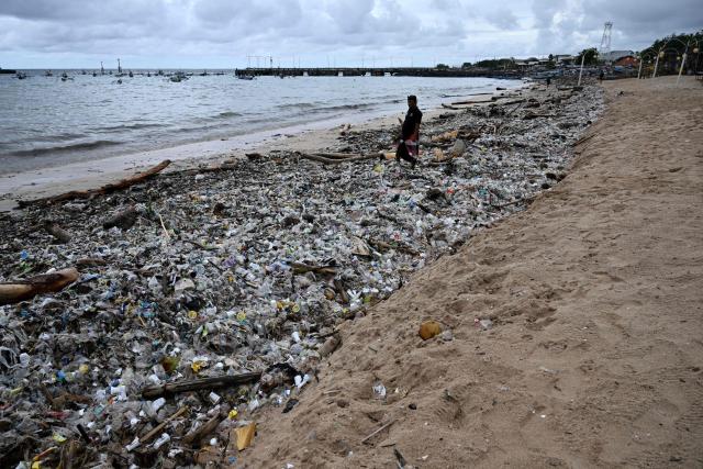 A man stands on plastic waste and other garbage washed ashore that has accumulated thickly at a beach in Kedonganan Badung regency, on the resort island of Bali on January 3, 2025. (Photo by SONNY TUMBELAKA / AFP)