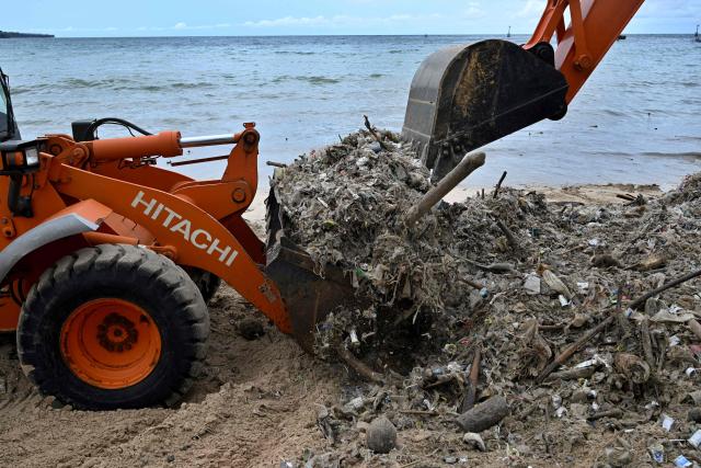 Workers clear plastic waste and other garbage washed ashore that has accumulated thickly at a beach in Kedonganan Badung regency, on the resort island of Bali on January 3, 2025. (Photo by SONNY TUMBELAKA / AFP)