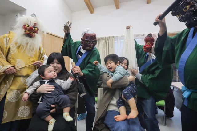 This photo taken on January 2, 2025 shows men in masks and costumes shouting loudly and startling children to drive away evil spirits for the "Noto no amamehagi" tradition, where participants go from house to house in the city of Wajima, Ishikawa prefecture, one year after an earthquake devastated the region. The quake on New Year's Day 2024 was Japan's deadliest in over a decade, claiming nearly 470 lives. (Photo by JIJI Press / AFP) / Japan OUT