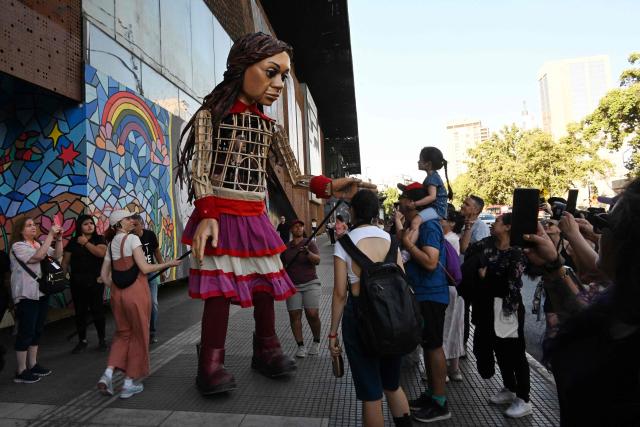 People interact with Little Amal, a 12-foot-tall puppet representing a ten-year-old Syrian refugee, during a performance at the Gabriel Mistral Cultural Center as part of the opening of the 32nd version of the International Festival Teatro a Mil in Santiago on January 3, 2025. Santiago a Mil International Theatre Festival is an annual performing arts festival that takes place in January in Santiago, Chile. It is the largest arts festival in Chile and includes theatre, dance, and music events from Chile and abroad, performed in the capital city, Santiago, and around the country. (Photo by RODRIGO ARANGUA / AFP)