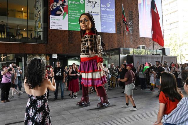 People look at Little Amal, a 12-foot-tall puppet representing a ten-year-old Syrian refugee, during a performance at the Gabriel Mistral Cultural Center as part of the opening of the 32nd version of the International Festival Teatro a Mil in Santiago on January 3, 2025. Santiago a Mil International Theatre Festival is an annual performing arts festival that takes place in January in Santiago, Chile. It is the largest arts festival in Chile and includes theatre, dance, and music events from Chile and abroad, performed in the capital city, Santiago, and around the country. (Photo by RODRIGO ARANGUA / AFP)