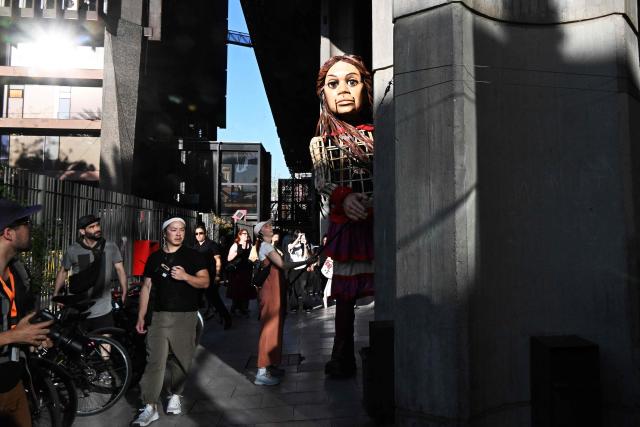 People look at Little Amal, a 12-foot-tall puppet representing a ten-year-old Syrian refugee, during a performance at the Gabriel Mistral Cultural Center as part of the opening of the 32nd version of the International Festival Teatro a Mil in Santiago on January 3, 2025. Santiago a Mil International Theatre Festival is an annual performing arts festival that takes place in January in Santiago, Chile. It is the largest arts festival in Chile and includes theatre, dance, and music events from Chile and abroad, performed in the capital city, Santiago, and around the country. (Photo by RODRIGO ARANGUA / AFP)