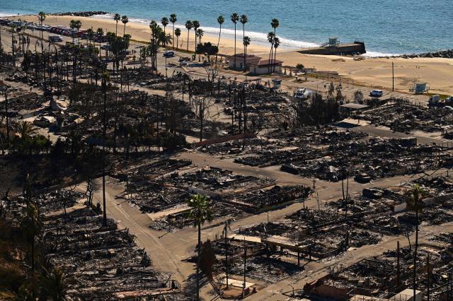 Charred homes and burnt cars are pictured amid the rubble of the fire-ravaged Pacific Palisades Bowl Mobile Estates in Los Angeles, California, on January 13, 2025. Firefighters were battling massive wildfires on January 13 that have ravaged Los Angeles and killed at least 24 people, with officials warning of incoming dangerous winds that could whip up the blazes further. (Photo by AGUSTIN PAULLIER / AFP)