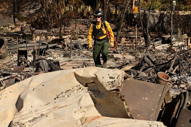 A firefighter looks through the remains of a house destroyed in the Palisades Fire in the Pacific Palisades neighborhood of Los Angeles, California, on January 13, 2025. Firefighters were battling massive wildfires on January 13 that have ravaged Los Angeles and killed at least 24 people, with officials warning of incoming dangerous winds that could whip up the blazes further. (Photo by AGUSTIN PAULLIER / AFP)