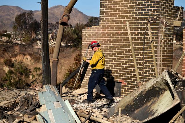 A firefighter looks through the remains of a house destroyed in the Palisades Fire in the Pacific Palisades neighborhood of Los Angeles, California, on January 13, 2025. Firefighters were battling massive wildfires on January 13 that have ravaged Los Angeles and killed at least 24 people, with officials warning of incoming dangerous winds that could whip up the blazes further. (Photo by AGUSTIN PAULLIER / AFP)