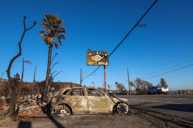 A charred vehicle is seen near the sign for Wylie's Bait & Tackle on Pacific Coast Highway on January 14, 2025, Malibu, California, in the aftermath of the Palisades Fire. Powerful winds forecast for late January 14 threatened to whip up massive fires that are still burning around Los Angeles in a tragedy that has killed at least 25 people and badly shaken the city. (Photo by VALERIE MACON / AFP)