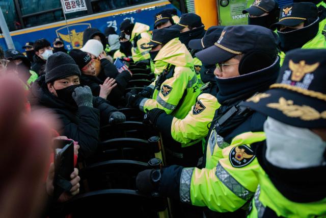 Police officers stand at the barricade with supporters of impeached South Korean President Yoon Suk Yeol as authorities try to detain him near his residence in Seoul on January 15, 2025. Yoon was arrested on January 15 over his failed martial law bid, after hundreds of anti-graft investigators and police raided his residence to end a weeks-long standoff. (Photo by YASUYOSHI CHIBA / AFP)