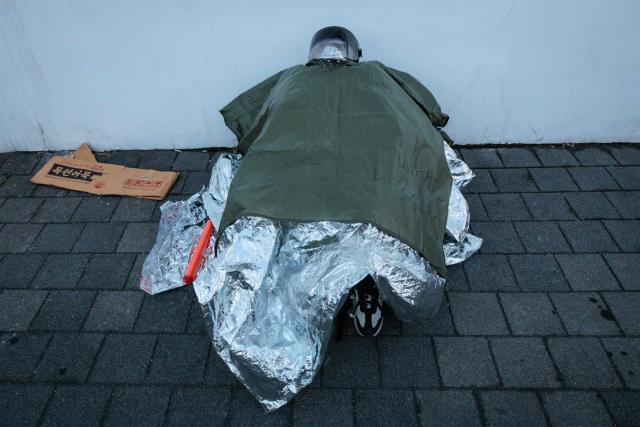 A supporter of impeached South Korean President Yoon Suk Yeol sleeps on a sidewalk as authorities try to detain him near his residence in Seoul on January 15, 2025. Yoon was arrested on January 15 over his failed martial law bid, after hundreds of anti-graft investigators and police raided his residence to end a weeks-long standoff. (Photo by YASUYOSHI CHIBA / AFP)