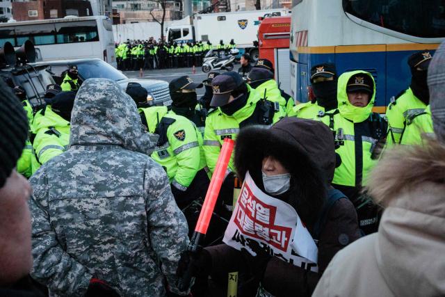 Police officers stand at the barricade with supporters of impeached South Korean President Yoon Suk Yeol as authorities try to detain him near his residence in Seoul on January 15, 2025. Yoon was arrested on January 15 over his failed martial law bid, after hundreds of anti-graft investigators and police raided his residence to end a weeks-long standoff. (Photo by YASUYOSHI CHIBA / AFP)