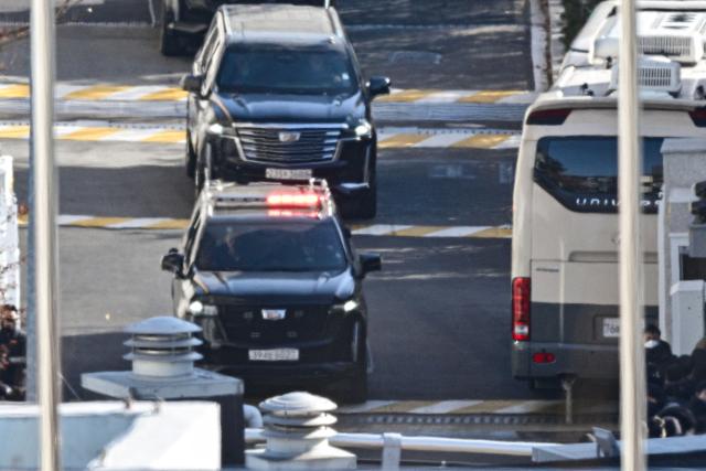 TOPSHOT - A vehicle (top) carrying South Korean impeached president Yoon Suk Yeol leaves his residence in Seoul on January 15, 2025. Yoon was arrested on January 15 over his failed martial law bid, after hundreds of anti-graft investigators and police raided his residence to end a weeks-long standoff. (Photo by ANTHONY WALLACE / AFP)