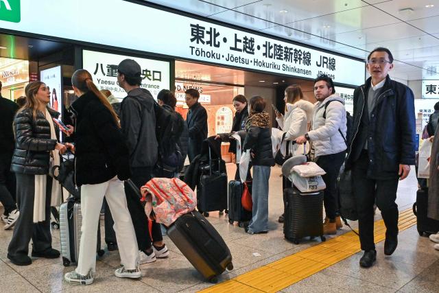 Travellers queue up with their bags to go through the gates of the high speed rail system at Tokyo station on January 15, 2025. Japan is expected to announce tourist figures for the year 2024 later in the day on January 15, widely expected to break the record set in 2019. (Photo by Richard A. Brooks / AFP)