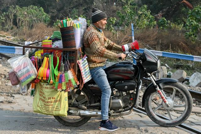 A vendor selling plastic items on a motorcycle crosses a railway track in Amritsar on January 15, 2025. (Photo by Narinder NANU / AFP)