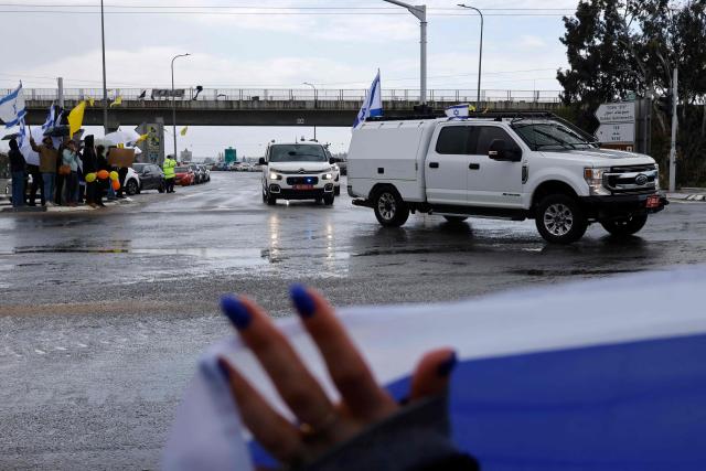 Israelis wave the national flag as convoy of vehicles transporting the bodies of the four Israeli hostages handed over by Hamas, drives near the southern city of Sderot on February 20, 2025. Hamas handed over on February 20 coffins believed to contain the bodies of four Israeli hostages, including those of the Bibas family who became symbols of the ordeal that has gripped Israel since the Gaza war began. The transfer of the bodies is the first by Hamas since its October 7, 2023 attack on Israel triggered the war, and is taking place under a fragile ceasefire that has seen living hostages exchanged for Palestinians held in Israeli prisons. (Photo by John Wessels / AFP)