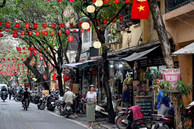 A tourist (C) takes a selfie under the national and communist party flags of Vietnam displayed along a street in Hanoi on March 13, 2025. (Photo by Nhac NGUYEN / AFP)