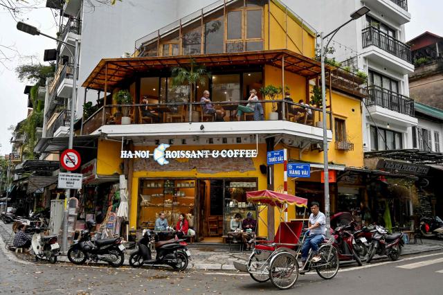 A driver rides his cyclo past a cafe in Hanoi on March 13, 2025. (Photo by Nhac NGUYEN / AFP)