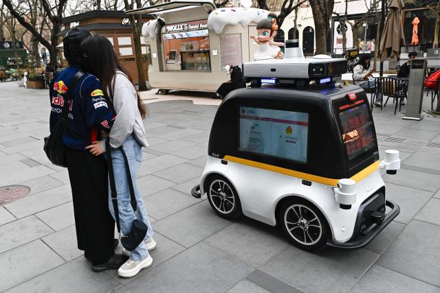 TOPSHOT - A self-driving police patrol vehicle moves past a couple at a shopping mall in Beijing on March 13, 2025. (Photo by Pedro PARDO / AFP)