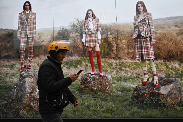 A food delivery man walks past an advertisement at a shopping mall in Beijing on March 13, 2025. (Photo by Pedro PARDO / AFP)