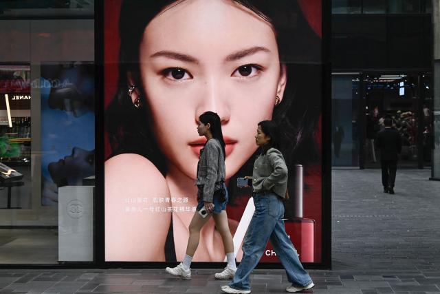 People walk past an advertisement at a shopping mall in Beijing on March 13, 2025. (Photo by Pedro PARDO / AFP)