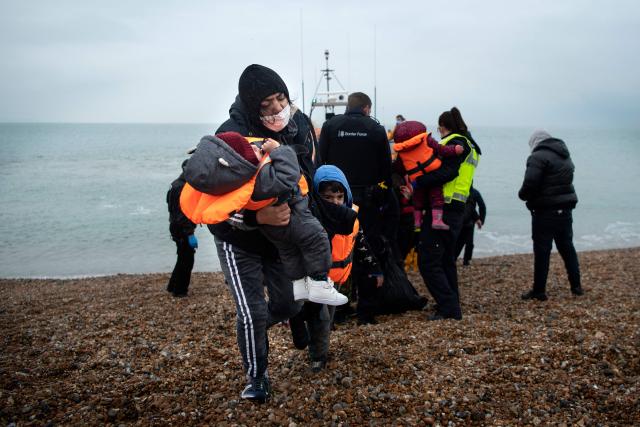 (FILES) A migrant carries her children after being helped ashore from a RNLI (Royal National Lifeboat Institution) lifeboat at a beach in Dungeness, on the south-east coast of England, on November 24, 2021, after being rescued while crossing the English Channel. A record number of migrants crossed the English Channel illegally on small boats to reach the UK in the first quarter of 2025, according to a count by AFP, based on data from the UK Home Office. Since January 1, 5,844 migrants have arrived illegally in the UK on makeshift boats, an all-time high for this time of year. Over the past week, 1,452 people arrived in the UK on these small boats, including 335 on March 23 alone. (Photo by Ben STANSALL / AFP)