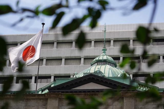 Japan’s national flag flutters in the wind on the Bank of Japan (BoJ) head office building in Tokyo on May 1, 2025. The Bank of Japan revised down its growth forecasts and held interest rates steady on May 1, warning that trade tariffs are fuelling global economic uncertainty. (Photo by Kazuhiro NOGI / AFP)
