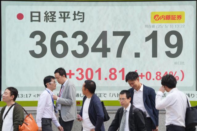 Pedestrians walk in front of an electronic quotation board displaying the Nikkei Stock Average on the Tokyo Stock Exchange in Tokyo on May 1, 2025. The Bank of Japan (BoJ) revised down its growth forecasts and held interest rates steady on May 1, warning that trade tariffs are fuelling global economic uncertainty. (Photo by Kazuhiro NOGI / AFP)