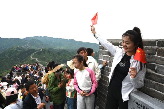 A woman poses with Chinese flags on the Great Wall of China at Badaling, north of Beijing, on May 1, 2025, the first day of a 5-day national May Day holiday. (Photo by GREG BAKER / AFP)