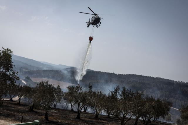 A helicopter drops water as it helps to extinguish fire at an olive tree garden near Latrun Monastery in central Israel, on May 1, 2025. Israeli firefighting teams battled wildfires near Jerusalem for a second day on May 1, with police reporting the reopening of several major roads that had been closed. (Photo by JOHN WESSELS / AFP)