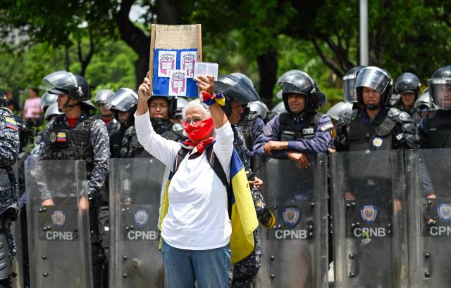 An opponent of the government of Venezuela's President Nicolas Maduro demonstrates in front of members of the Bolivarian National Police during a Labor Day protest in Caracas on May 1, 2025. A group of public workers and pensioners protested in Caracas on Thursday to demand a "living wage," hours after President Nicolas Maduro announced an increase in pensions and bonuses received by public employees. (Photo by Juan BARRETO / AFP)