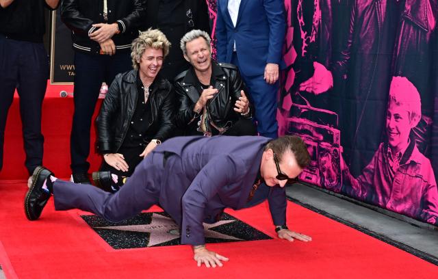 Green Day's Tre Cool (C) lays in front of Billie Joe Armstrong and Mike Dirnt on their newly unveiled star on the Hollywood Walk of Fame during a ceremony in Hollywood, California, on May 1, 2025. (Photo by Frederic J. BROWN / AFP)