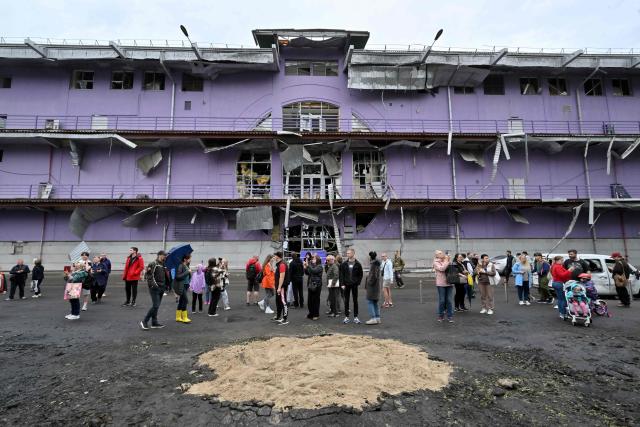 People arrive to look at the damage to a shopping mall as they stand close to a crater filled with fresh sand following a night-time drone attack on Kyiv, on May 4, 2025 amid the Russian invasion of Ukraine. (Photo by Sergei SUPINSKY / AFP)