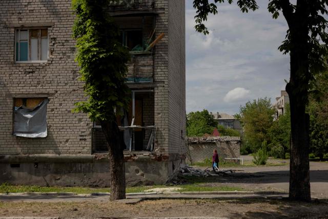 A woman walks near a damaged residential building in the town of Lyman, near the frontline in the Donetsk region, on May 7, 2025 amid the Russian invasion of Ukraine. (Photo by Tetiana DZHAFAROVA / AFP)