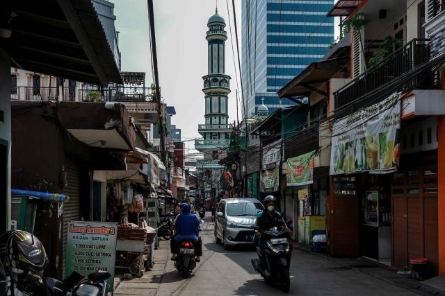 People commute past businesses in an alley in Jakarta on May 9, 2025. (Photo by BAY ISMOYO / AFP)