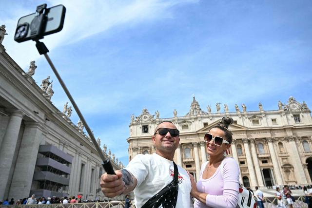 Visitors use a smartphone with a selfie stick at St Peter's Square with the St Peter's Basilica in the background in The Vatican on May 9, 2025. (Photo by Gabriel BOUYS / AFP)