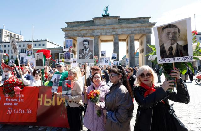 People hold photographs of fallen soldiers as they walk from Brandenburg Gate (seen in the background) towards the Soviet War Memorial in Berlin's Tiergarten district to attend celebrations to mark the 80th anniversary of the Soviet Union's victory over Nazi Germany in the Second World War (WWII) on May 9, 2025. (Photo by Odd ANDERSEN / AFP)
