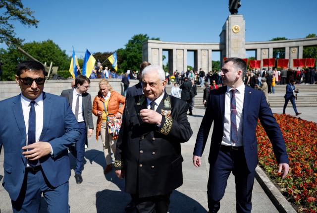 People wave Ukrainian flags (L, background) as Russia's ambassador to Germany Sergey Nechayev (C) leaves after visiting the Soviet War Memorial in Berlin's Tiergarten district during celebrations to mark the 80th anniversary of the Soviet Union's victory over Nazi Germany in the Second World War (WWII) on May 9, 2025. (Photo by Odd ANDERSEN / AFP)