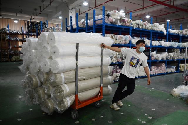 A worker hauls rolls of fabric after unloading them at a warehouse in a textile industrial park in Shaoxing, in China’s eastern Zhejiang province on May 9, 2025. China and the US will hold trade talks in Switzerland this weekend - the first since Donald Trump unveiled sweeping tariffs that shook global markets. (Photo by GREG BAKER / AFP)