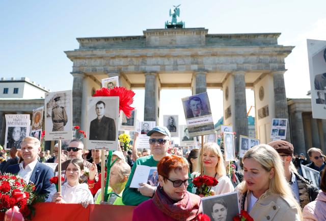 People hold photographs of fallen soldiers as they walk from Brandenburg Gate (seen in the background) towards the Soviet War Memorial in Berlin's Tiergarten district to attend celebrations to mark the 80th anniversary of the Soviet Union's victory over Nazi Germany in the Second World War (WWII) on May 9, 2025. (Photo by Odd ANDERSEN / AFP)