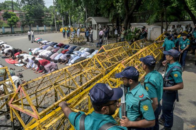 Bangladesh Police personnel stand guard as protesters offer Friday prayers near the State Guest House Jamuna, the official residence of Bangladesh's Chief Advisor Office of Interim Government Muhammad Yunus, demanding a ban on the ousted Sheikh Hasina’s party, the Awami League, in Dhaka on May 9, 2025. (Photo by Munir UZ ZAMAN / AFP)
