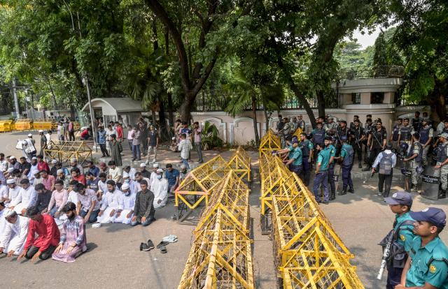Bangladesh Police personnel stand guard as protesters offer Friday prayers near the State Guest House Jamuna, the official residence of Bangladesh's Chief Advisor Office of Interim Government Muhammad Yunus, demanding a ban on the ousted Sheikh Hasina’s party, the Awami League, in Dhaka on May 9, 2025. (Photo by Munir UZ ZAMAN / AFP)