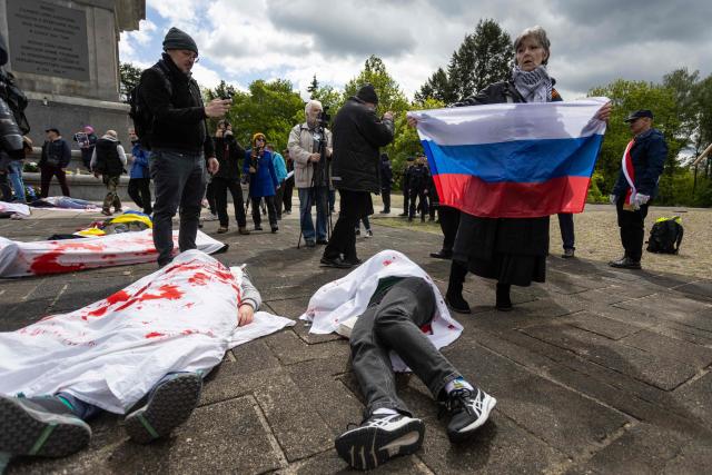 A woman with the Russian national flag reacts as Ukrainian activists lie on the pavement, simulating the bodies of victims, to protest the full-scale Russian invasion of Ukraine, at the mausoleum of Soviet soldiers in Warsaw, Poland, on May 9, 2025. (Photo by Wojtek RADWANSKI / AFP)