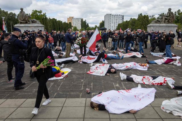 A woman with flowers passes by as Ukrainian activists lie on the pavement, simulating the bodies of victims, to protest the full-scale Russian invasion of Ukraine, at the mausoleum of Soviet soldiers in Warsaw, Poland, on May 9, 2025. (Photo by Wojtek RADWANSKI / AFP)