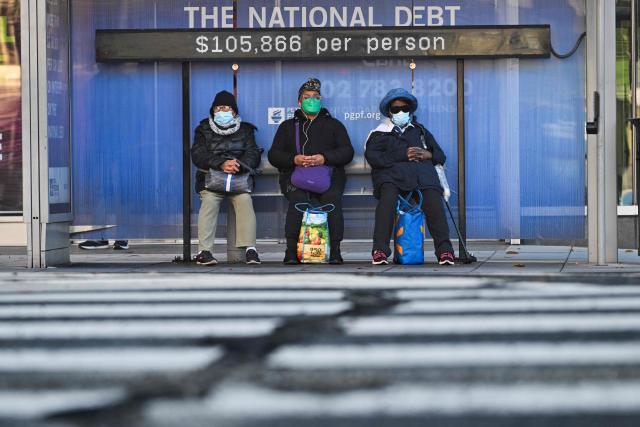 (FILES) Commuters wait at a bus stop where there is a National Debt Clock running totals that show the gross US national debt and each family's share of the debt in Washington, DC, on December 30, 2024. There is a "reasonable probability" the US will hit its borrowing limit in August when Congress is in recess, US Secretary of Treasury Scott Bessent said on May 9, 2025, calling on lawmakers to act. "I respectfully urge Congress to increase or suspend the debt limit by mid-July, before its scheduled break, to protect the full faith and credit of the United States," he wrote in a letter to US Speaker of the House Mike Johnson. (Photo by ROBERTO SCHMIDT / AFP)