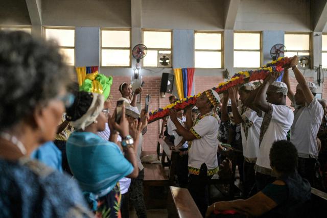 Men wearing typical dresses carry a cross inside a church during a mass as part of the celebration of Afro-Venezuelan Day in Caucagua, Miranda state, Venezuela on May 10, 2025. Afro-Venezuelan Day is celebrated in Venezuela on May 10, commemorating the heritage and cultural contributions of the Venezuelan Afro-descendant community, as well as their struggle and resistance against slavery. (Photo by Juan BARRETO / AFP)