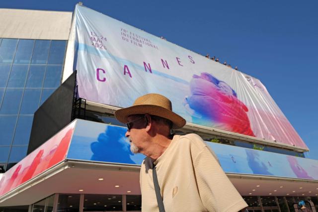 A local resident walks past the workers who install the official poster of the 78th Cannes Film Festival on the facade of the Palais des Festivals in Cannes, south-eastern France, on May 11, 2025. The 78th Cannes Film Festival will take place from May 13 to May 24, 2025. (Photo by Valery HACHE / AFP)
