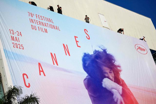 Workers hang the official poster of the 78th Cannes Film Festival on the facade of the Palais des Festivals in Cannes, south-eastern France, on May 11, 2025. Cannes Film festival will take place from May 13 to May 24. (Photo by Valery HACHE / AFP)