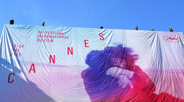 Workers hang the official poster of the 78th Cannes Film Festival on the facade of the Palais des Festivals in Cannes, south-eastern France, on May 11, 2025. Cannes Film festival will take place from May 13 to May 24. (Photo by Valery HACHE / AFP)