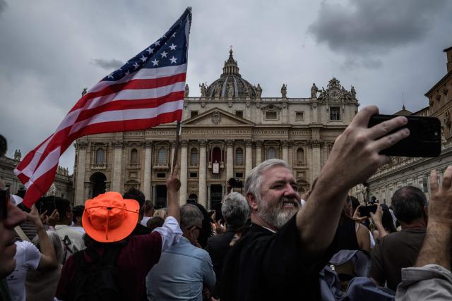 A faithful waves a US flag as another takes a selfie while Pope Leo XIV delivers the Regina Caeli prayer from the main central loggia of St Peter's basilica in The Vatican, on May 11, 2025. (Photo by JEFF PACHOUD / AFP)